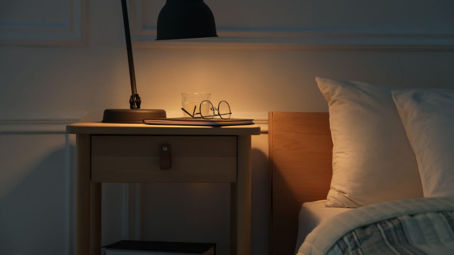 Table de chevet avec une lampe à lumière tamisée et un livre, près d'un lit